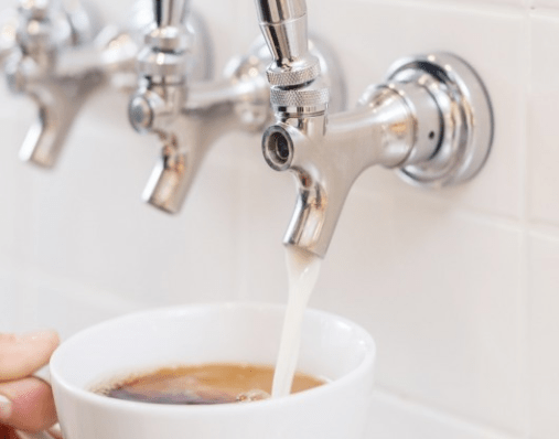 milk from a tap poured into a cup of coffee